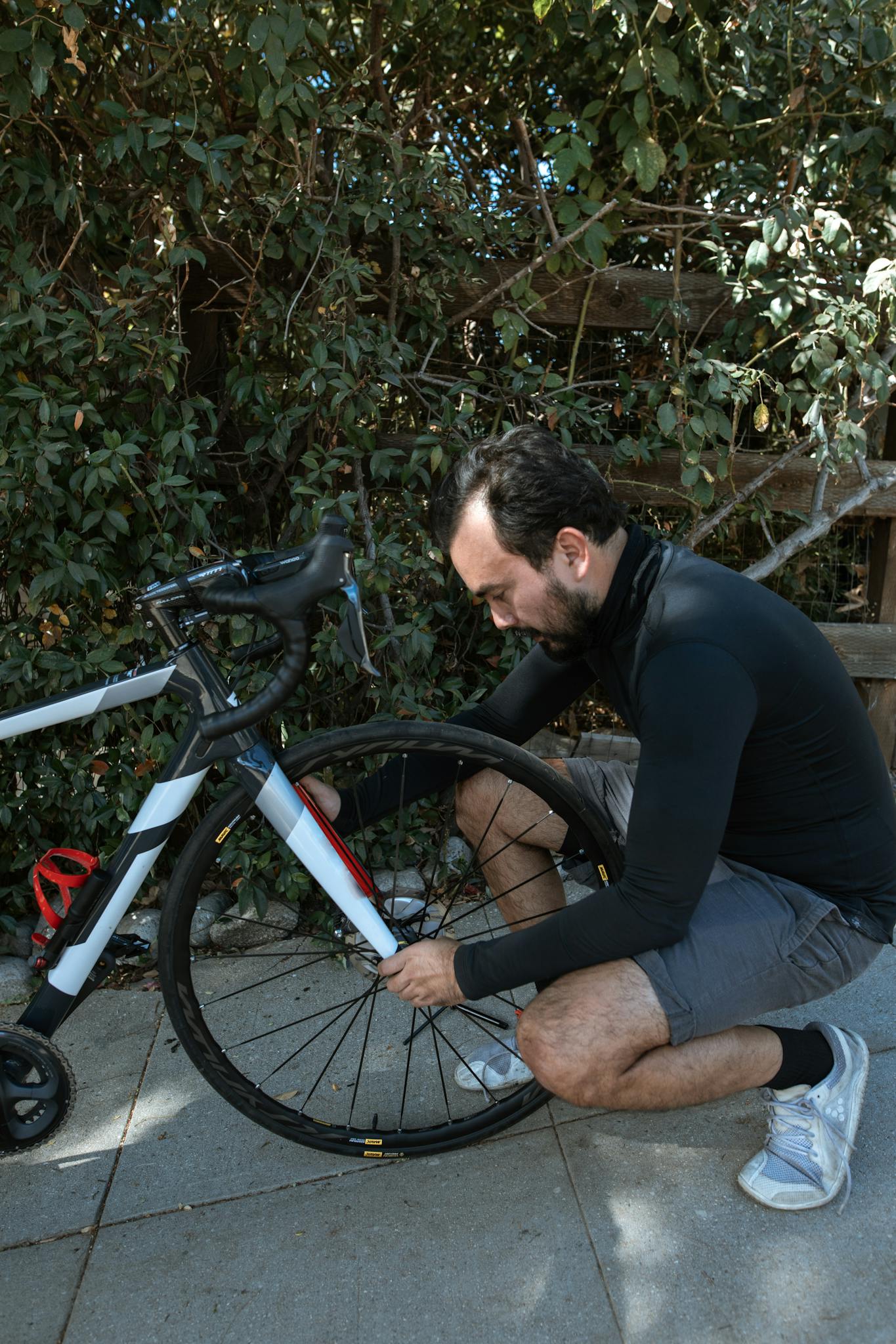 A man kneels to repair a bicycle tire, surrounded by lush greenery, illustrating outdoor activity.